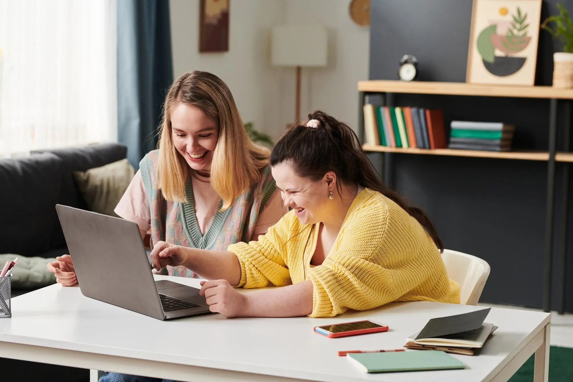 Disabled down syndrome girl watching something on laptop and laughing together with carer